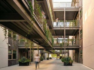 Industrial courtyard with steel walkways, cascading vines, planters, and blurred figures walking
