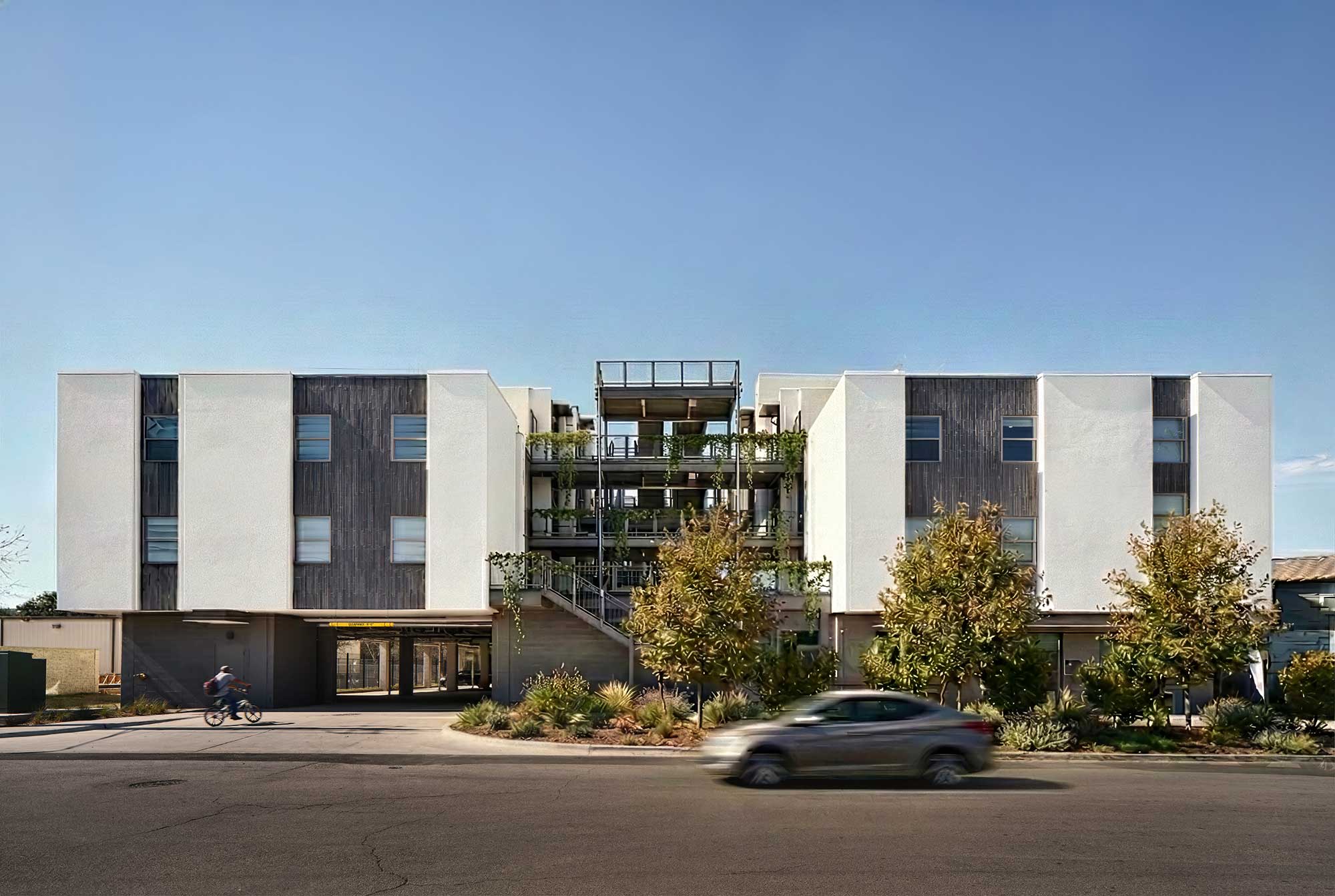 Modern mixed-use building with white stucco and dark wood facade, central stairway with greenery,