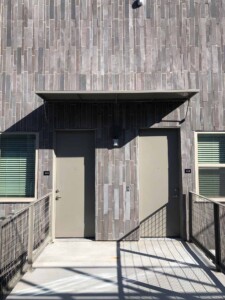 Modern apartment entrance with two beige doors, vertical stone tile cladding, metal awning and