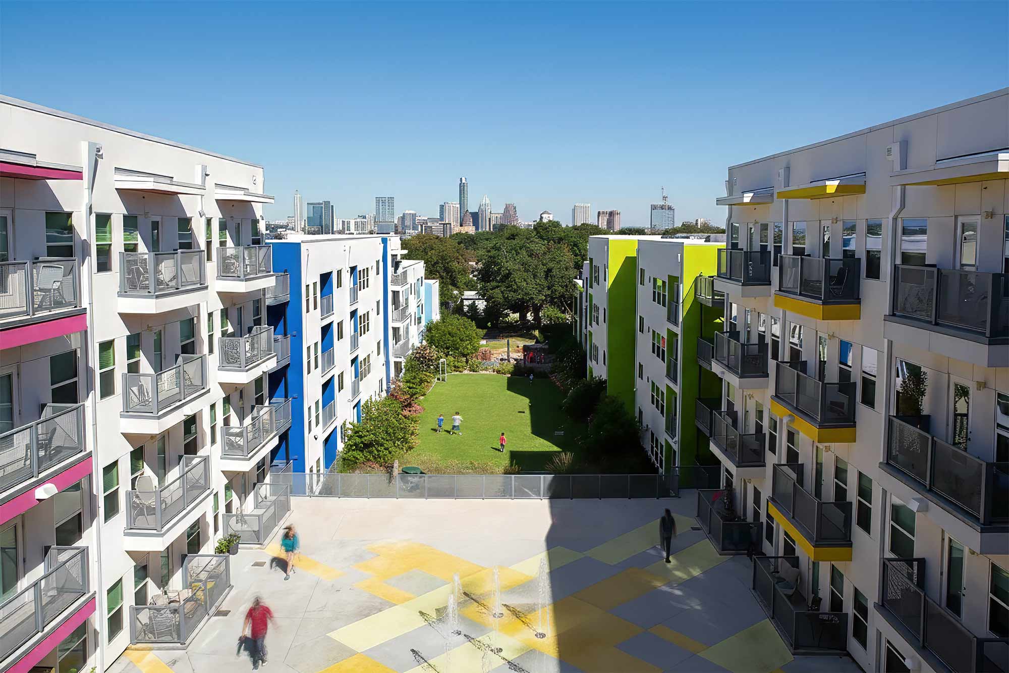 Modern apartment complex courtyard with colorful accent walls, balconies, green lawn and city