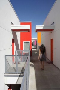 Person walking through modern housing complex corridor with white walls and colorful red orange
