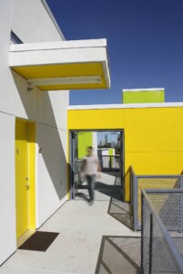 Person walking through outdoor corridor with white walls yellow accents and perforated metal