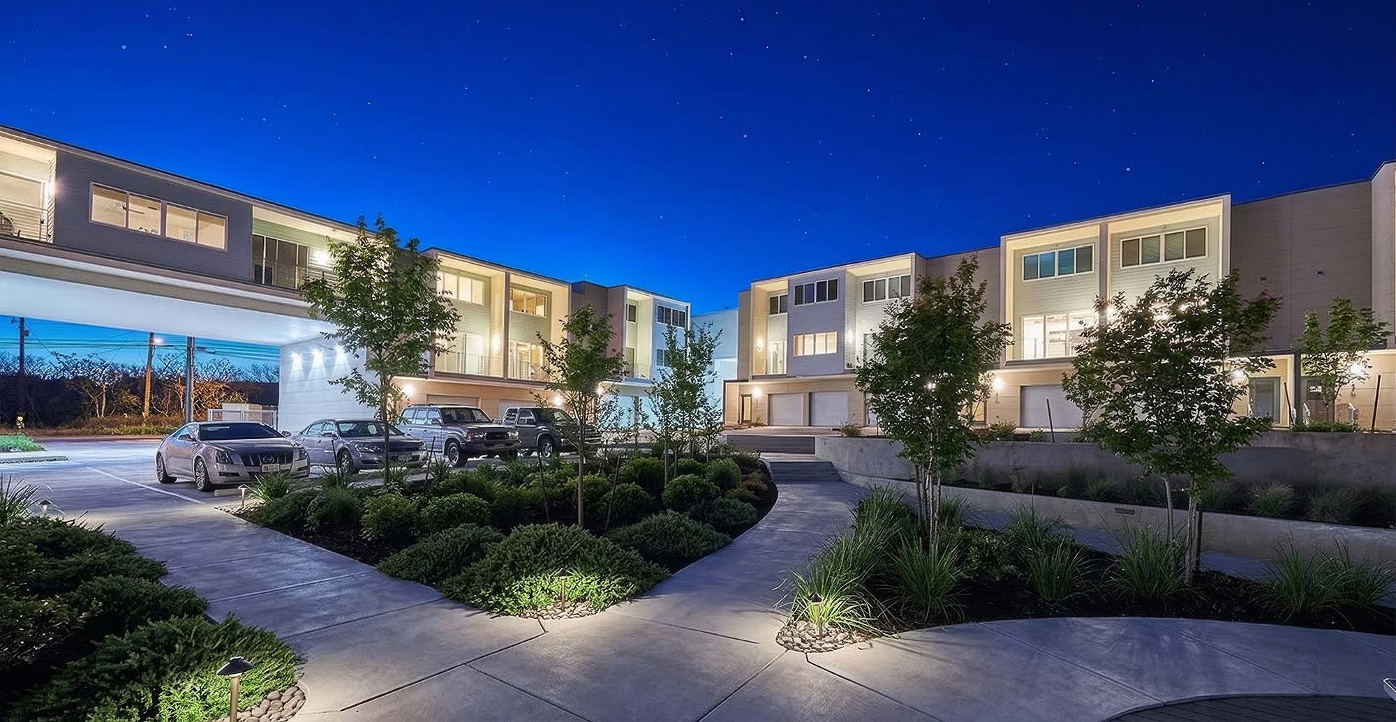 Modern townhouse complex at dusk with landscaped courtyard pathways and parked cars under starry sky