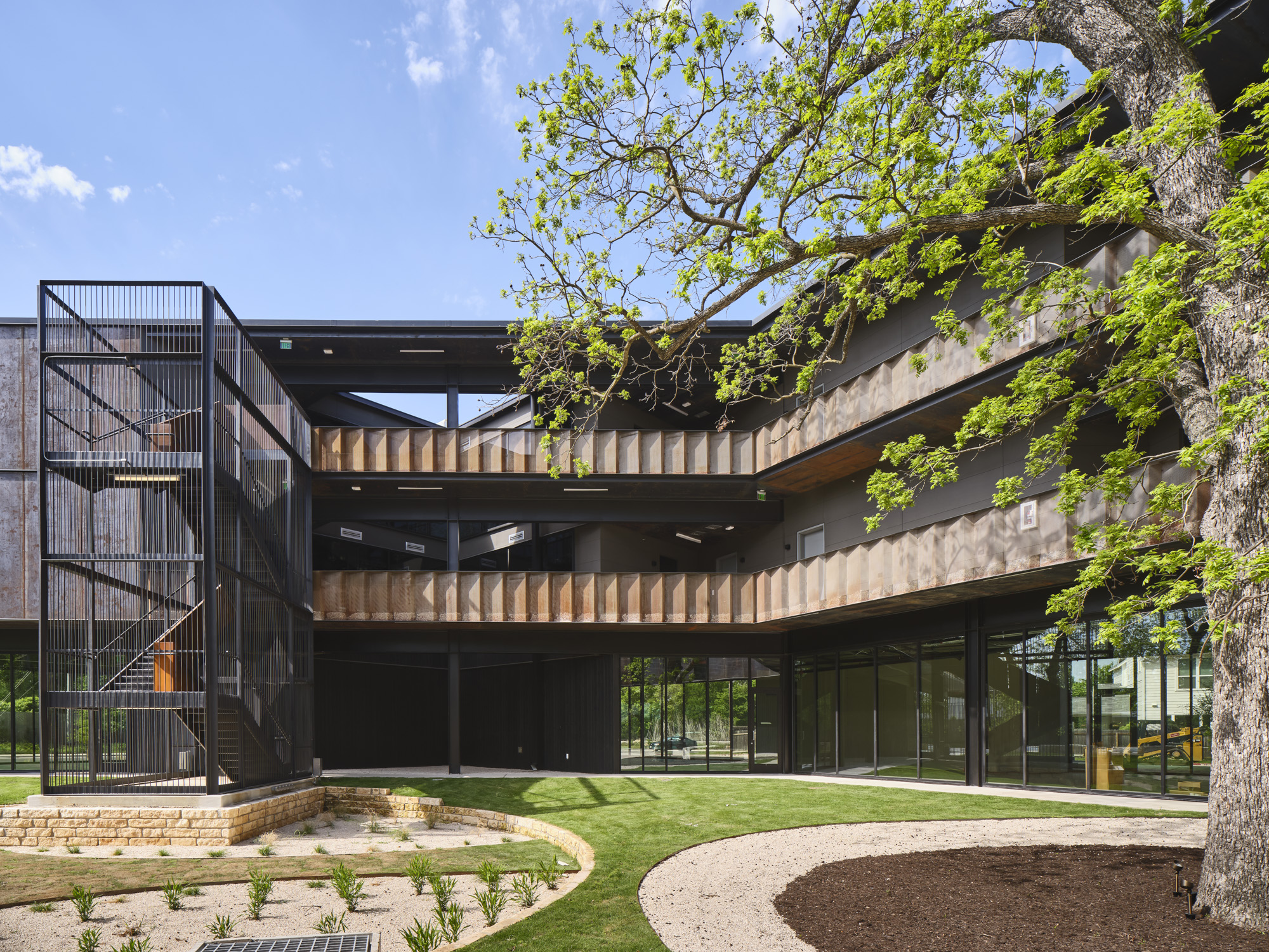 Three-story modern building with black steel staircase, wood balconies, glass walls and courtyard