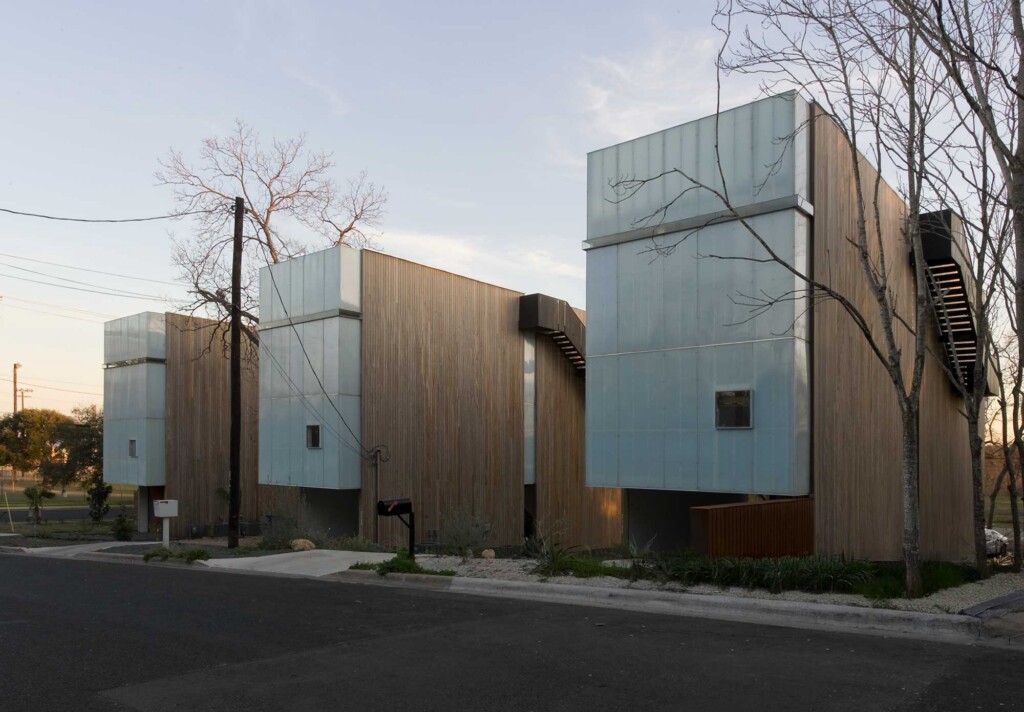 Modern townhouses with wood siding and metal-clad upper volumes along a residential street at dusk