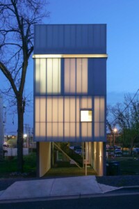 Modern elevated rectangular building with translucent panel facade glowing at dusk on stilts