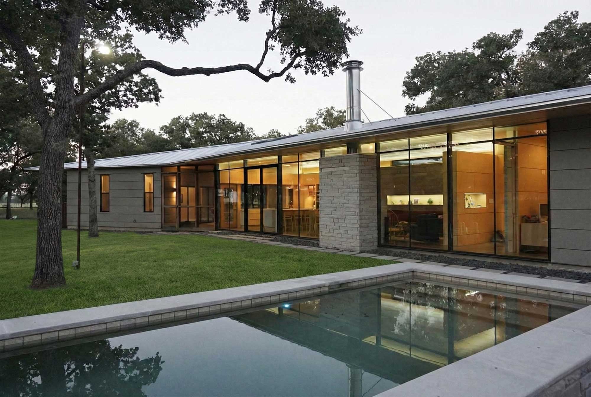 Modern ranch house with metal roof stone accents floor-to-ceiling windows pool and mature oak trees