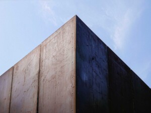 Corner view of weathered steel building facade against blue sky with visible panel fasteners