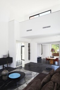 Modern open-plan living space with double-height white walls, polished concrete floors, and dining