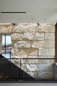 Interior staircase with rough-cut limestone wall glass railing and view to outdoor deck beyond