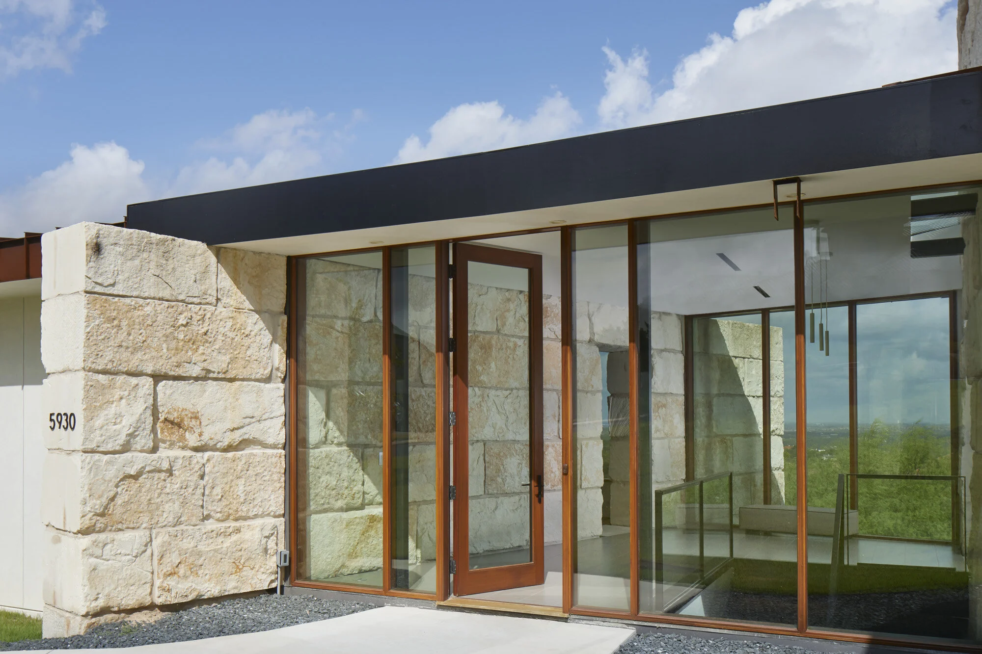 Modern entrance with limestone walls, wood-framed glass doors, flat black roof overhang and gravel