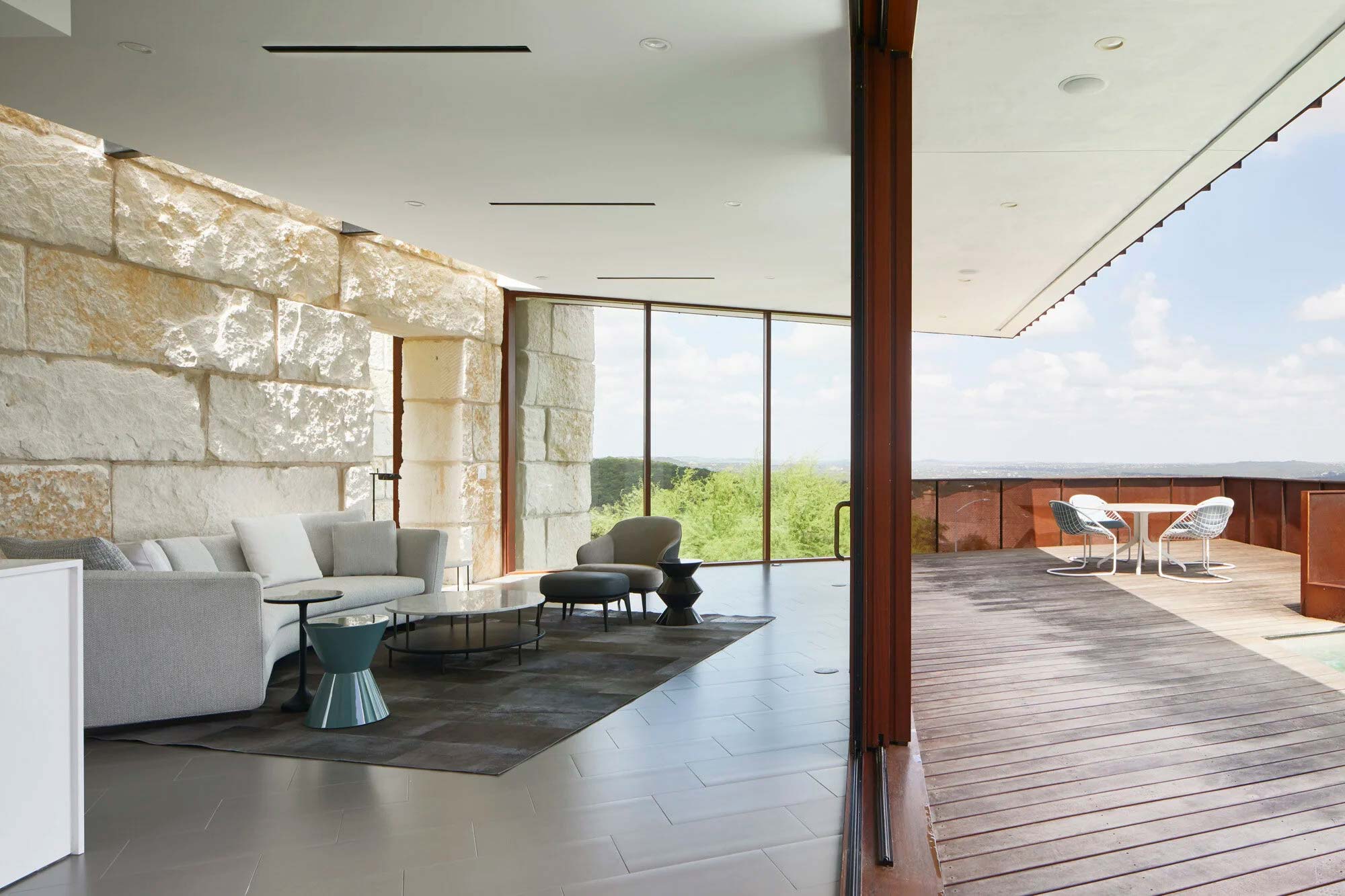 Modern living room with limestone wall opening to wood deck terrace with corten steel railing and