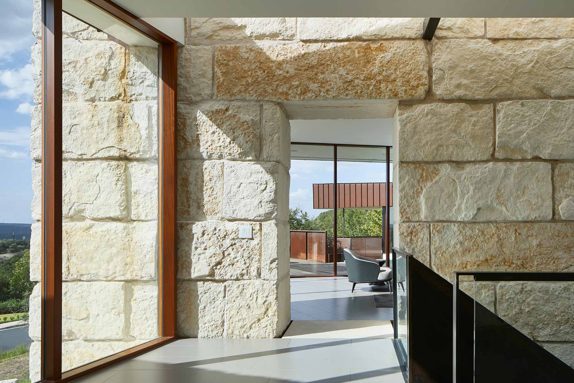 Interior hallway with rough-cut limestone walls, wood-framed window, and view to outdoor terrace