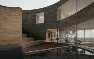Curved modern residence with dark stone and tan brick walls, wooden deck over reflecting pool,