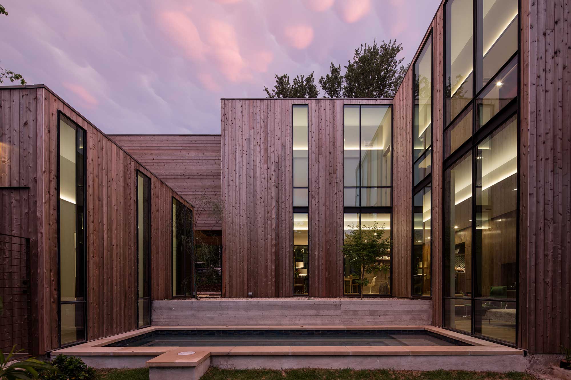 Modern wood-clad house with tall vertical windows, courtyard pool, and warm interior lighting at