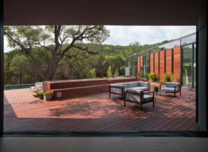 Modern wood deck with outdoor seating overlooking pool and forested hillside with horizontal slat