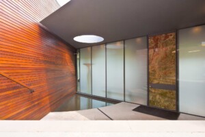 Modern entrance with horizontal wood siding, frosted glass panels, stone door, and circular skylight