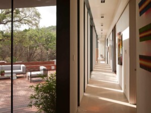 Long modern hallway with floor-to-ceiling windows overlooking wooden deck and trees with outdoor