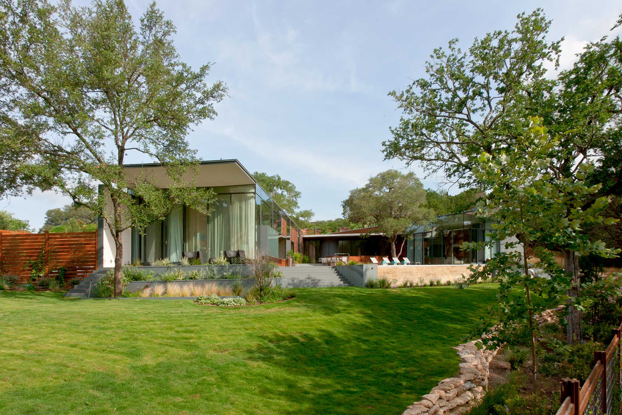 Modern glass and steel home with expansive lawn surrounded by mature oak trees and native