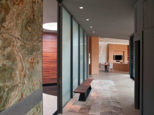 Modern hallway with green onyx wall, frosted glass panels, wooden bench, and view to open living
