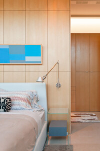 Modern bedroom with light wood paneled walls, blue abstract art, upholstered bed, glass nightstand
