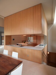 Modern kitchen with warm wood cabinetry, white countertops, and pass-through opening to dining area