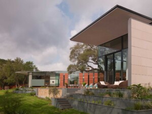 Modern home exterior with flat roofs, glass walls, wood siding, terraced landscaping and lawn