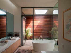Modern bathroom with freestanding white tub, wood slat privacy wall, skylights, and indoor plants
