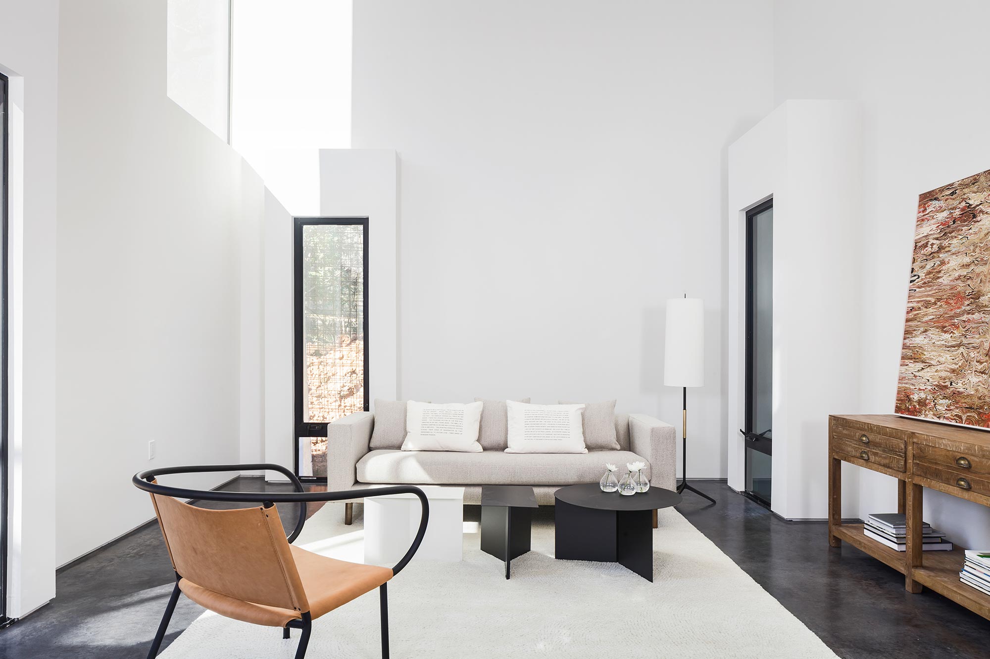 Minimalist living room with white walls, high clerestory windows, concrete floor, neutral sofa and