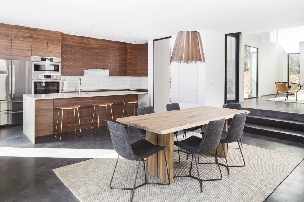 Modern open-plan kitchen and dining area with walnut cabinets, concrete floors, and natural wood