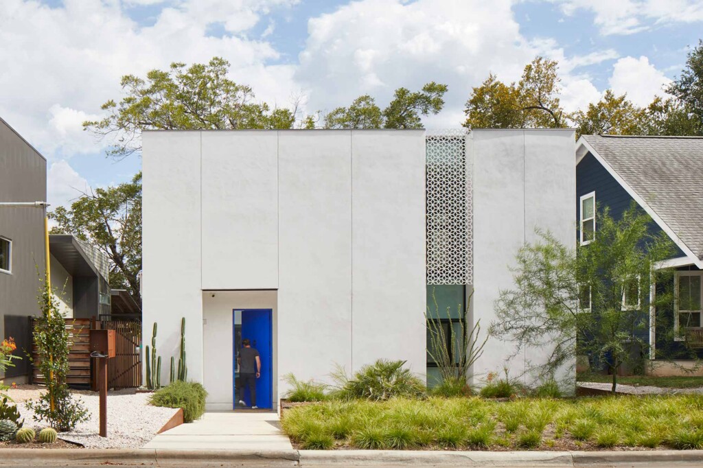 Modern white stucco home with blue door, decorative screen panel, desert landscaping, person