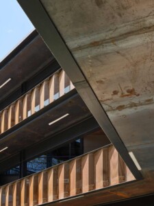 Steel and timber architectural detail showing angled beams with perforated copper screens and raw