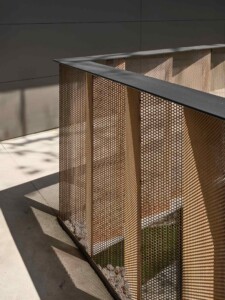 Perforated bronze metal screen enclosure with geometric folds casting intricate shadows on concrete