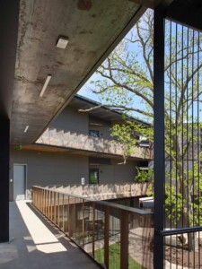 Covered walkway with concrete ceiling and perforated metal railings overlooking courtyard with
