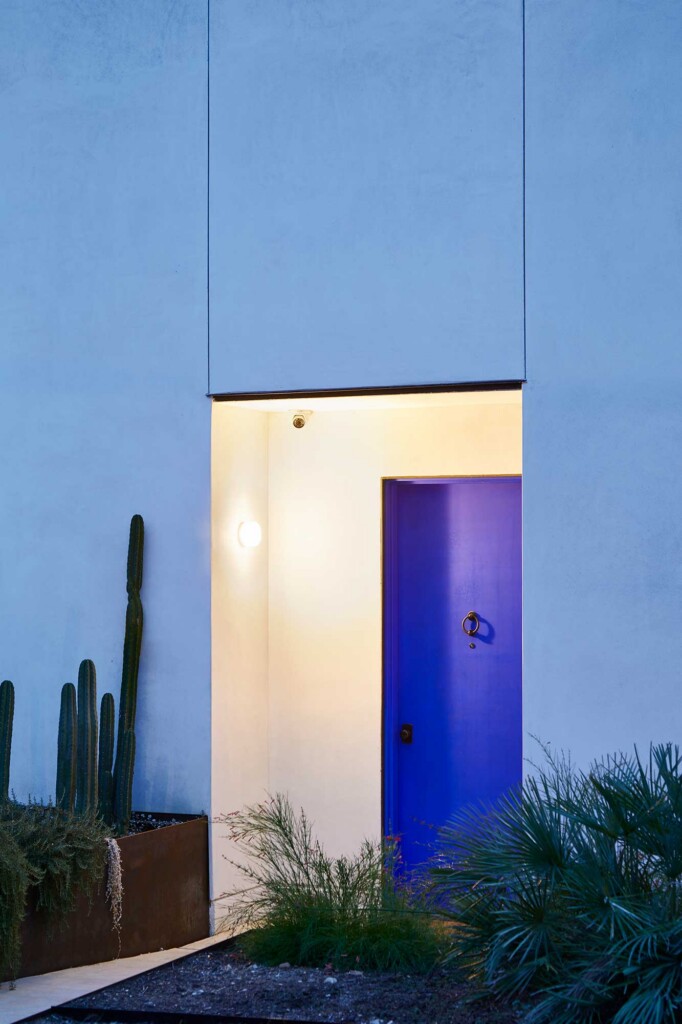 Blue stucco building entrance with vibrant cobalt door recessed alcove cacti and desert landscaping
