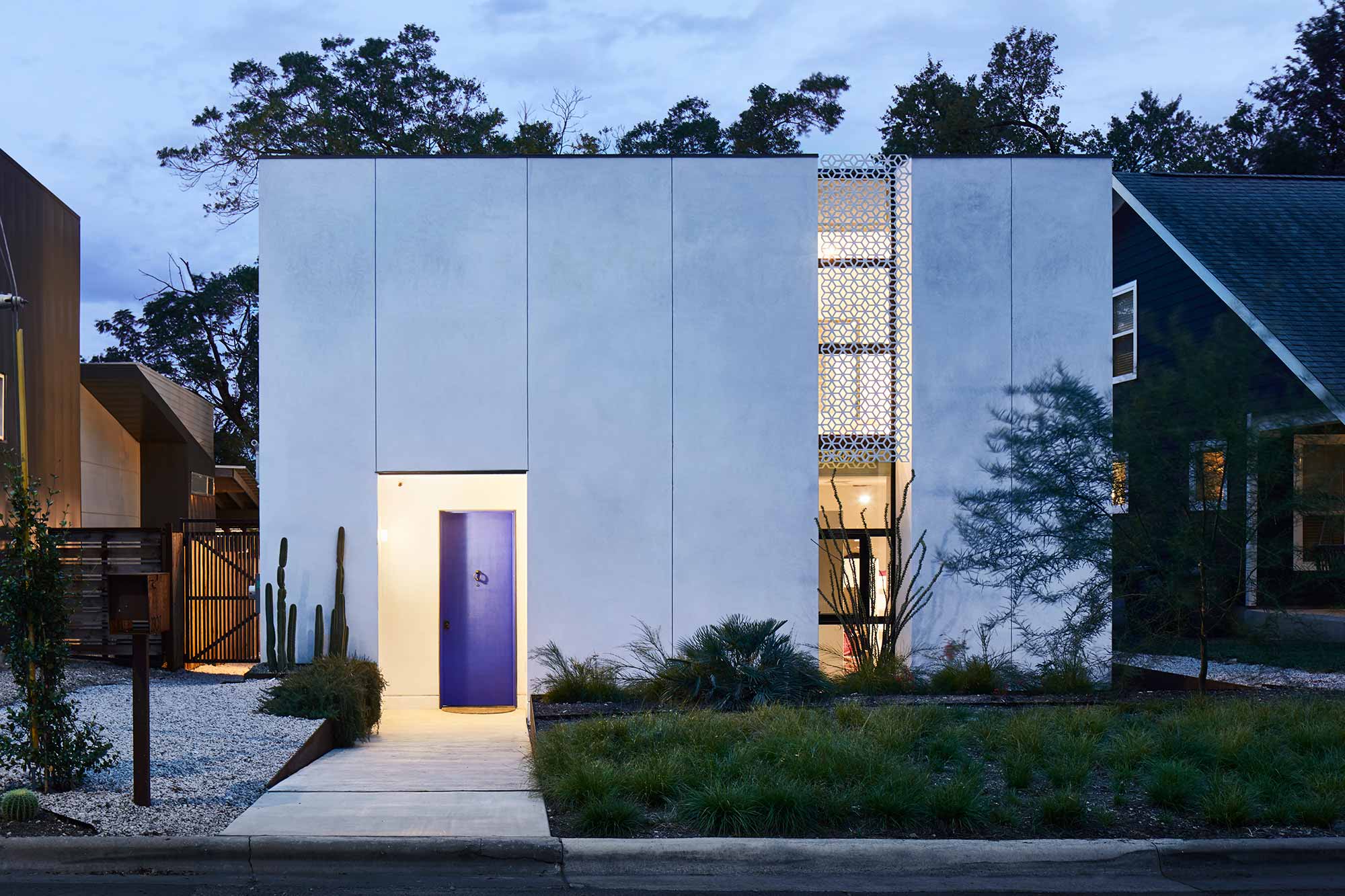 Modern white cubic house with purple door, decorative metal screen, desert landscaping at dusk