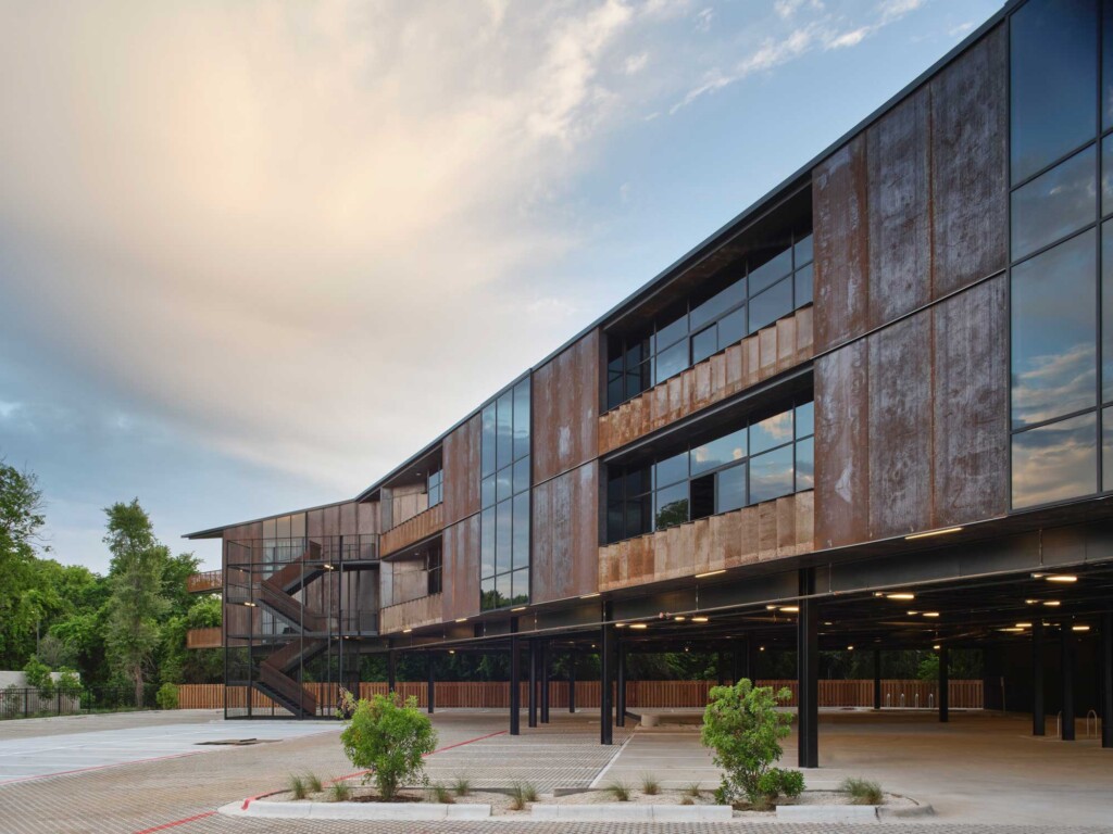 Industrial-style three-story building with weathered corten steel cladding and large glass windows