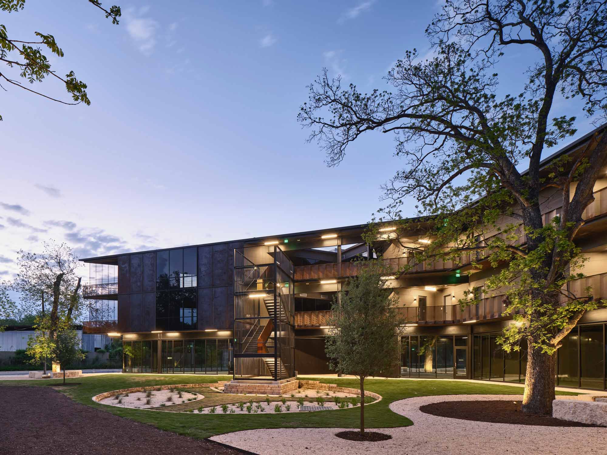 Modern three-story building with dark metal cladding, external staircase, and landscaped courtyard