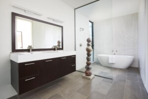 Modern bathroom with dark wood floating vanity, freestanding tub, glass partition, and decorative