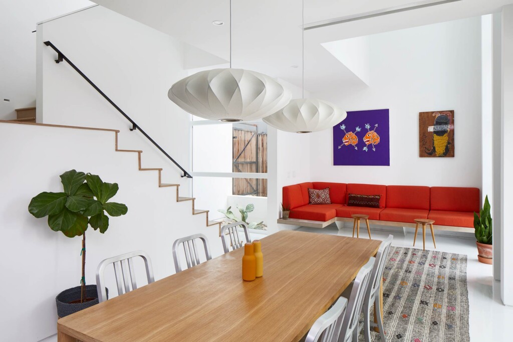 Open-plan living dining area with wood table white chairs red sectional sofa staircase and pendant