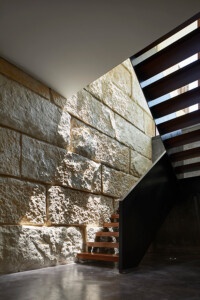 Modern staircase with floating wooden treads against textured stone wall and black steel structure