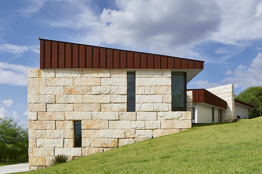 Modern home with limestone block walls and rust-colored metal roof set into grassy hillside