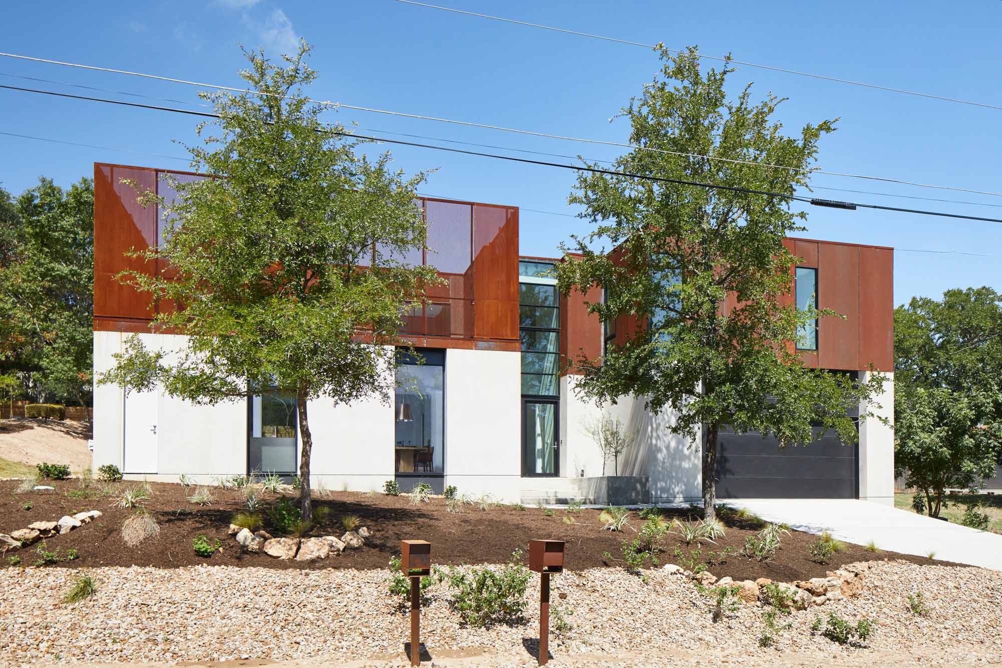 Modern two-story home with white stucco base and corten steel upper volumes surrounded by native