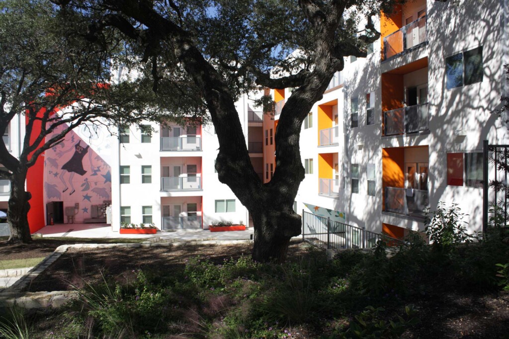 Colorful apartment building courtyard with mature oak trees, murals, and orange-accented balconies