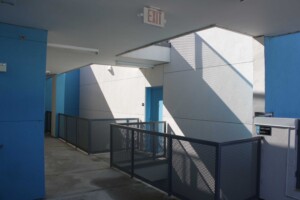 Covered walkway with blue accent walls, metal mesh railing, white stucco walls and angular shadows