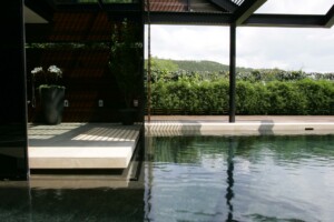 Modern pool pavilion with dark steel frame, stone deck, white orchid, bamboo hedge and hill views