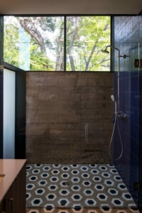 Modern shower with geometric blue hexagon floor tiles, raw concrete wall, blue tile accent, large