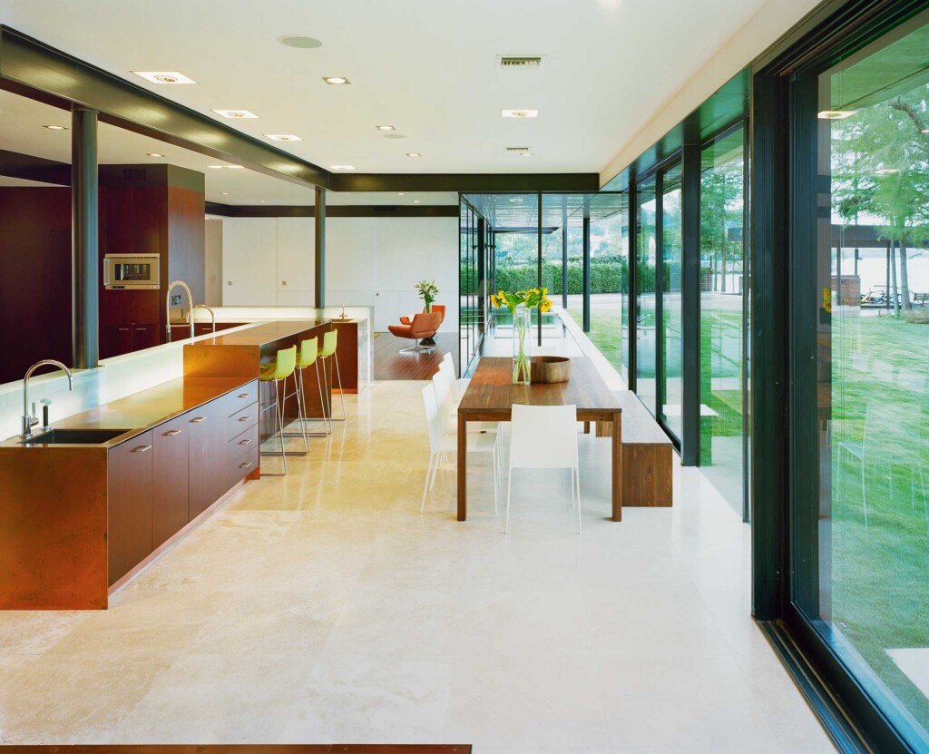 Modern open-plan kitchen and dining area with floor-to-ceiling glass walls overlooking green lawn