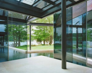 Modern glass pavilion with steel frame, reflecting pool, and views to lakeside lawn with trees