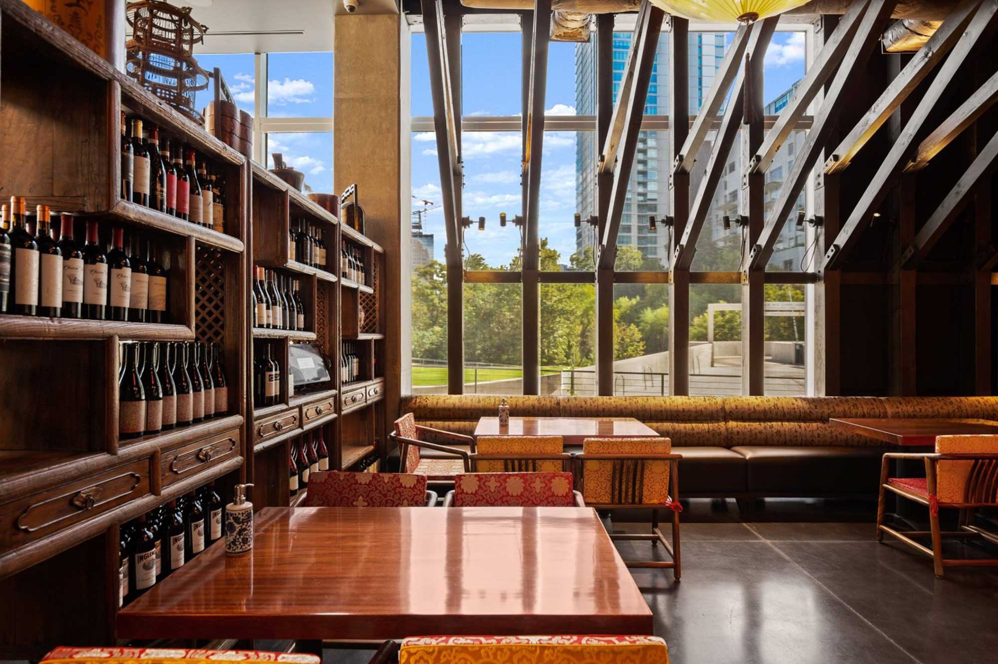 Restaurant interior with wine shelving, wooden tables, colorful chairs, and floor-to-ceiling windows